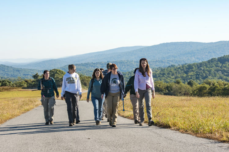 Students walk up path carrying telemetry equipment with mountains in background