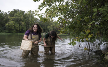 Two young women wade through a river