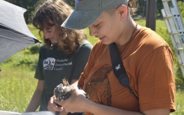 Student holding a bird while another student reviews data